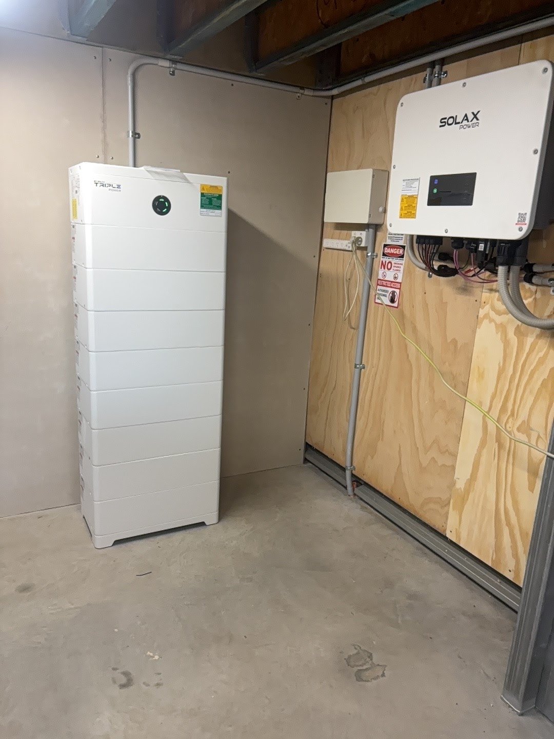SolaX X3-Ultra 20KP three-phase hybrid inverter and eight-module T51 battery stack on a garage wall — a real BD NRG install